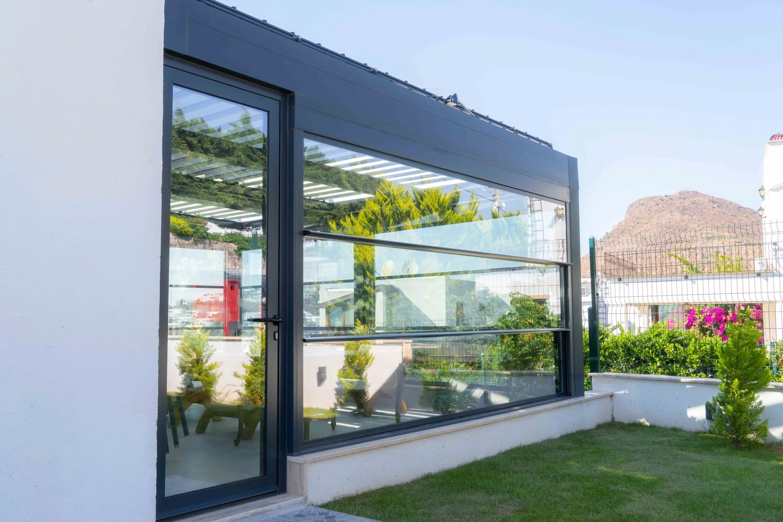 Side of a black framed home, with a glass door and a glass wall and a desert view